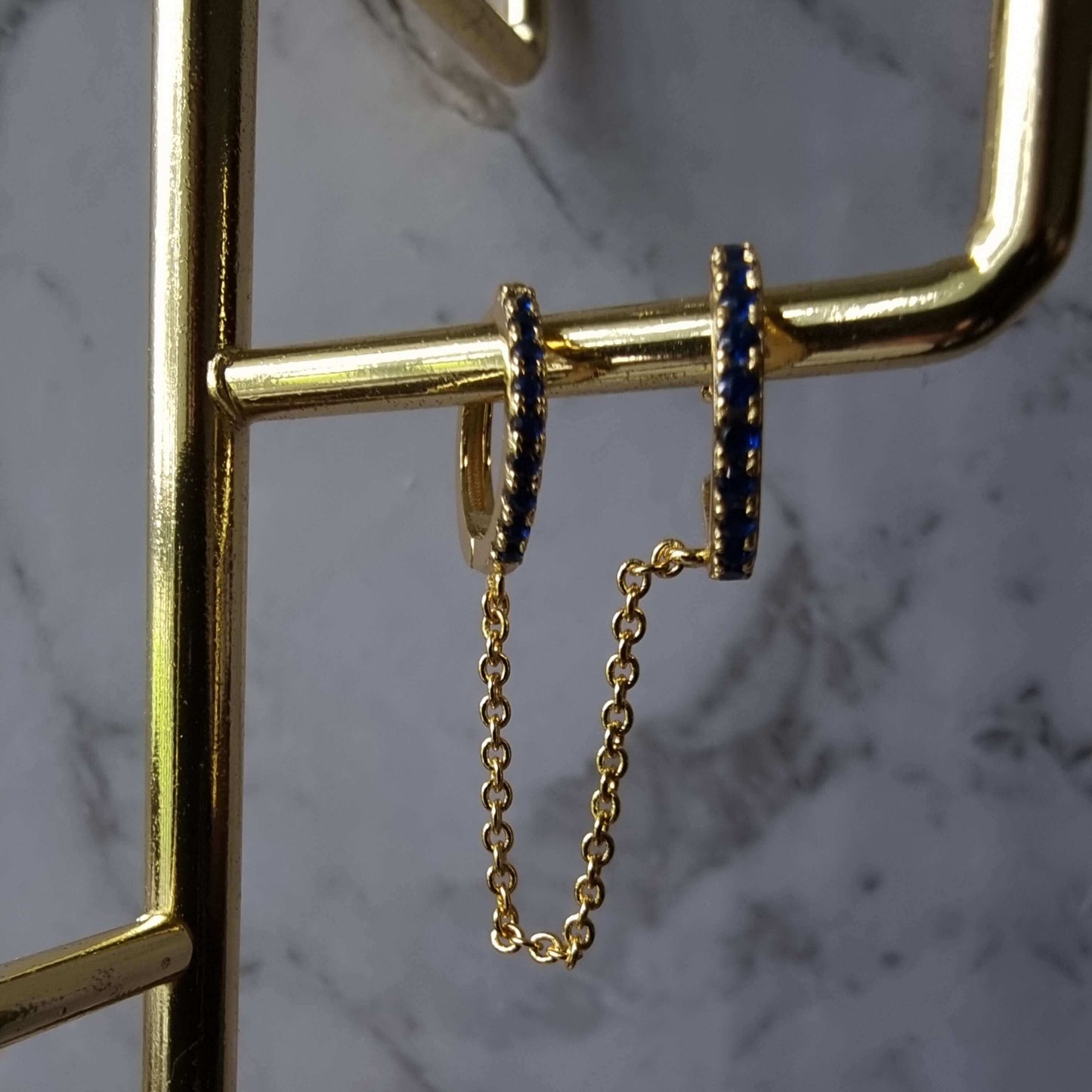 Detailed view of hoop to cuff chain ear piercing in 925 sterling silver with 18K gold plating and royal blue cubic zirconia centerpiece.