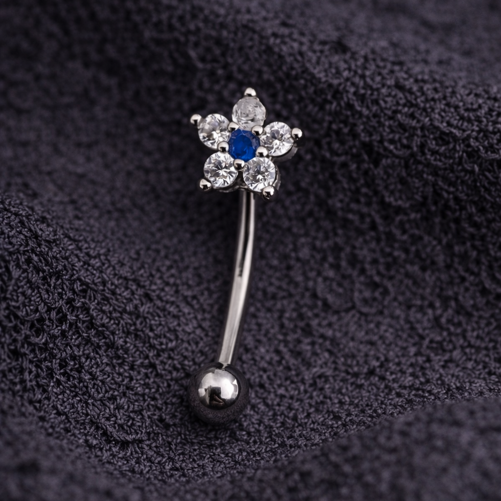 Belly eyebrow/rook barbell flower-shaped design and blue gemstone on a dark fabric background