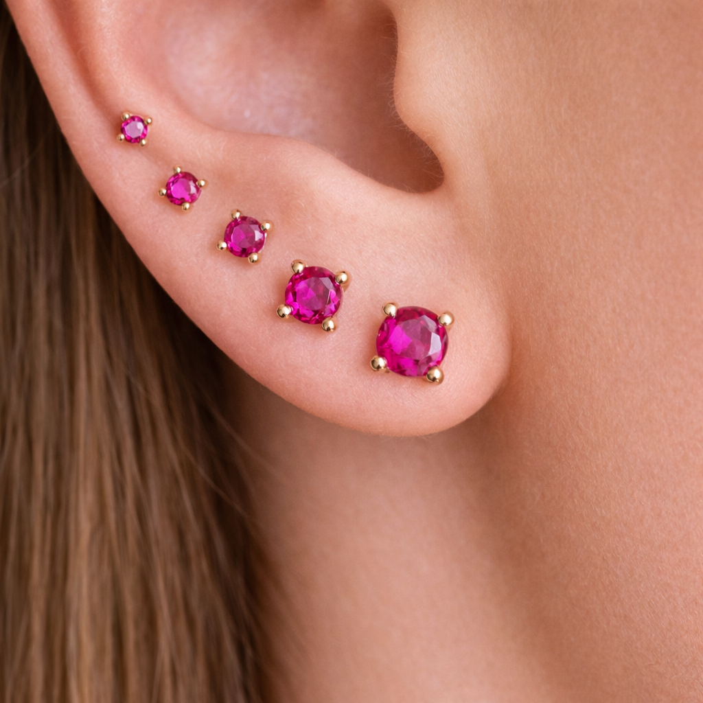 Close-up of an ear with pink gemstone earrings on a neutral background