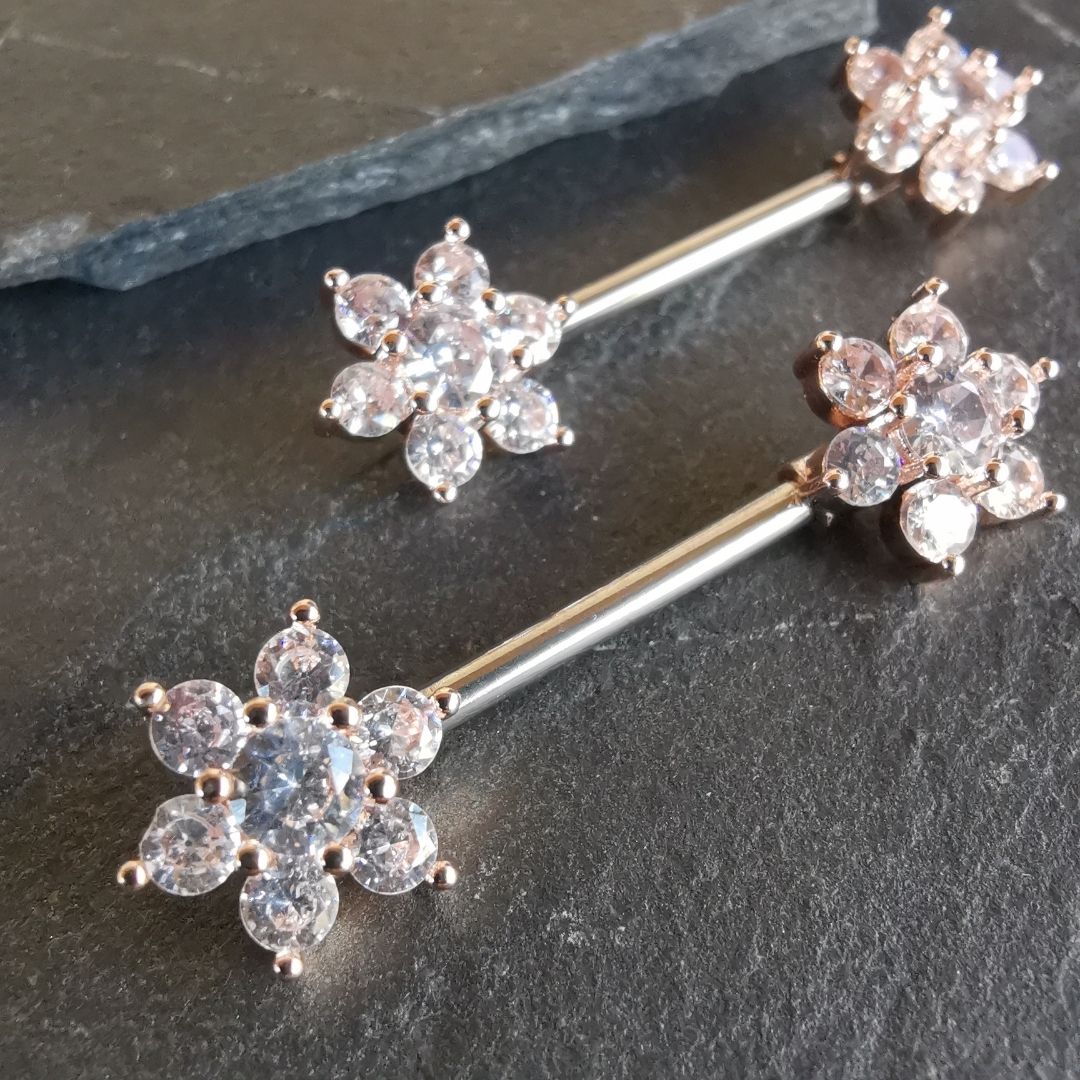 14G rose gold surgical steel nipple bar with a flower design and cubic zirconia accents.