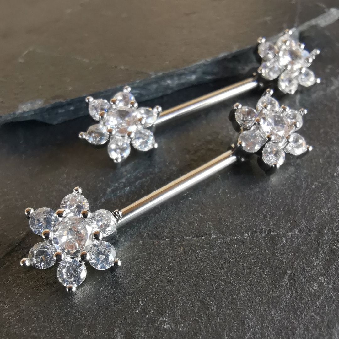 14G surgical steel nipple bar in silver with a flower design and sparkling cubic zirconia stones.