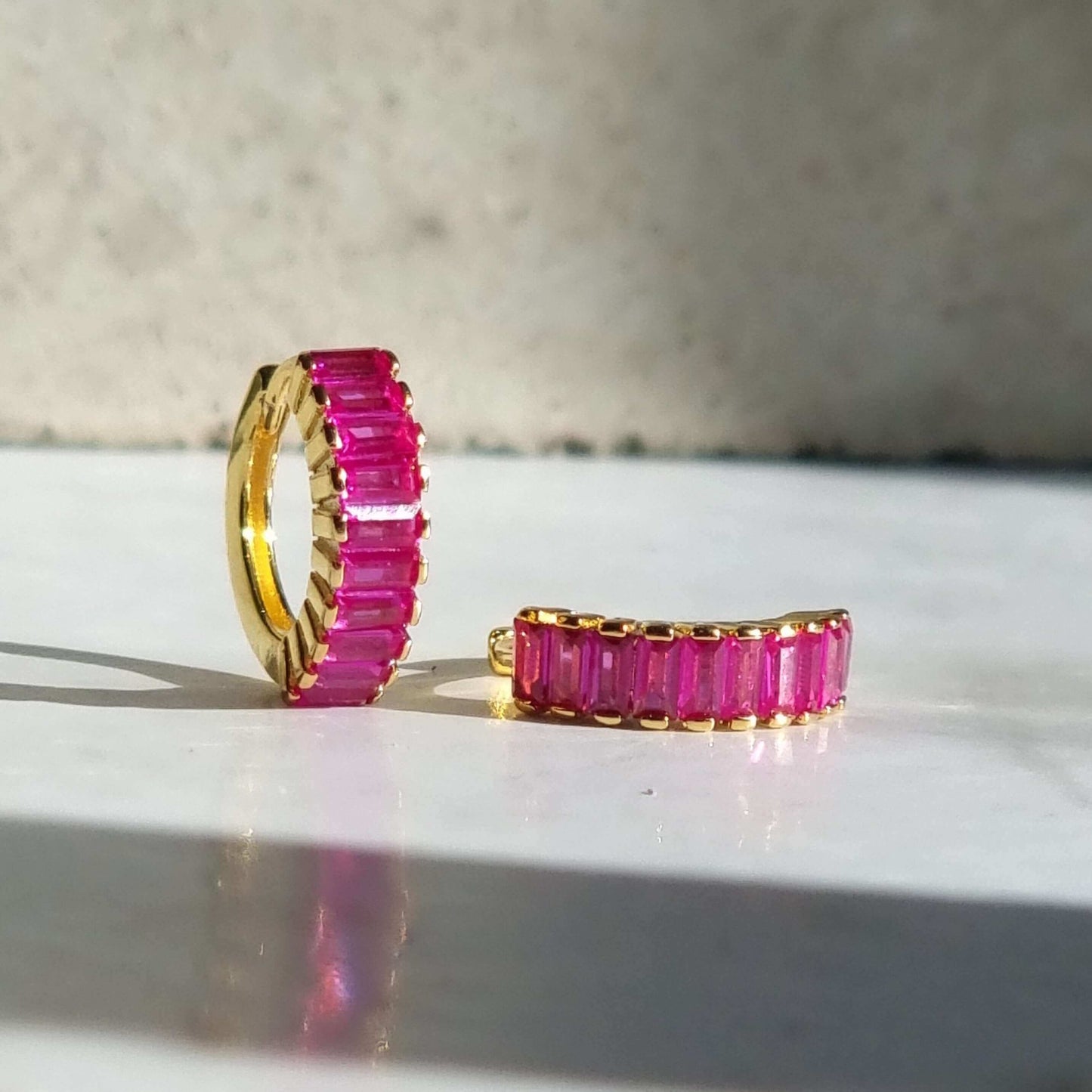 Side view of 18K gold-plated huggie earrings with magenta zirconia, highlighting the secure hinge clasp and minimalist modern silhouette.