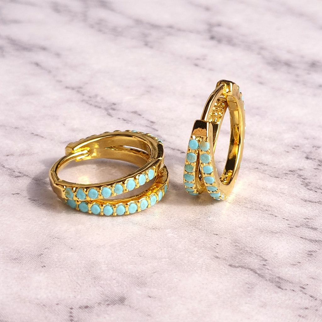 Gold hoop earrings with turquoise stones on a marble surface