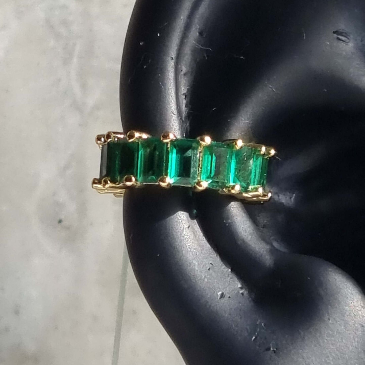 Minimalist gold ear cuff with bright green cubic zirconia, crafted in 18K gold-plated copper and designed for unpierced conch ear placement.
