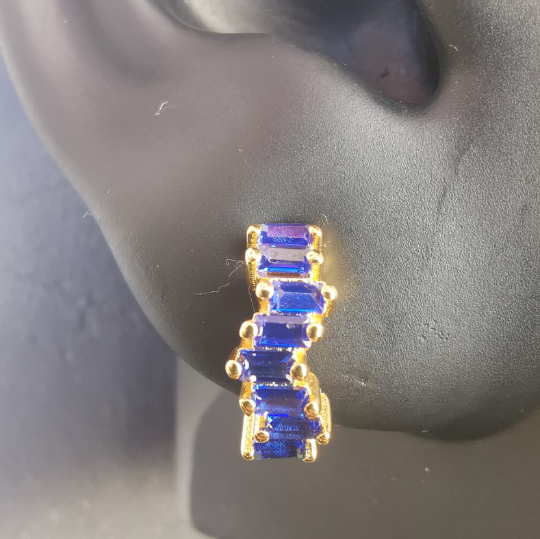 Close-up of huggie hoop earrings with deep royal blue zirconia stones set in 18K gold-plated sterling silver, showcasing high-polish finish and bold color.