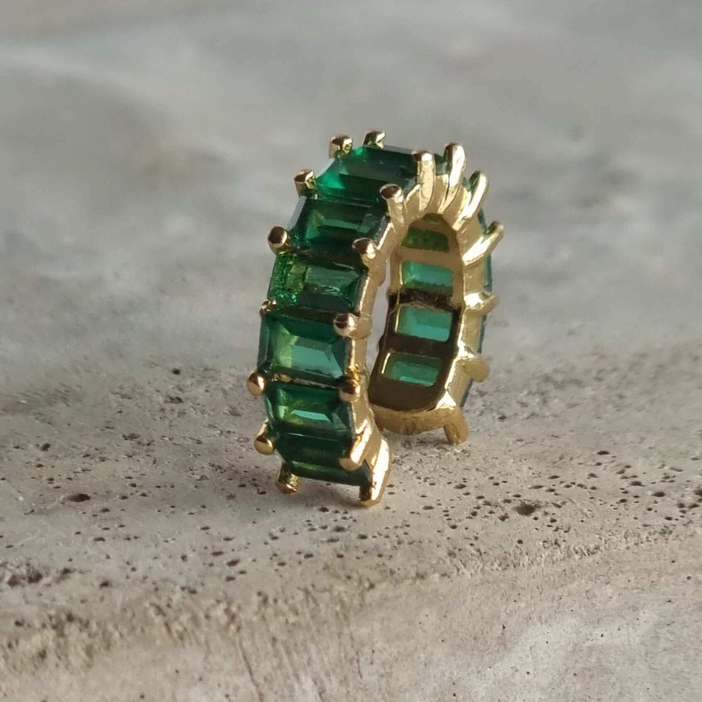 Close-up of 18K gold-plated ear cuff with vibrant green gemstone, designed to be worn on the conch without requiring a piercing.