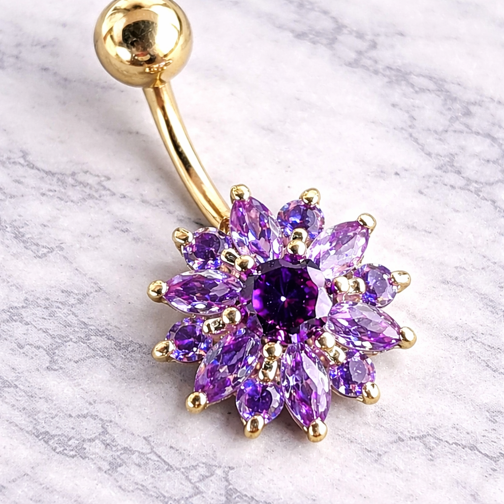 Gold belly button ring with purple gemstones on a marble background