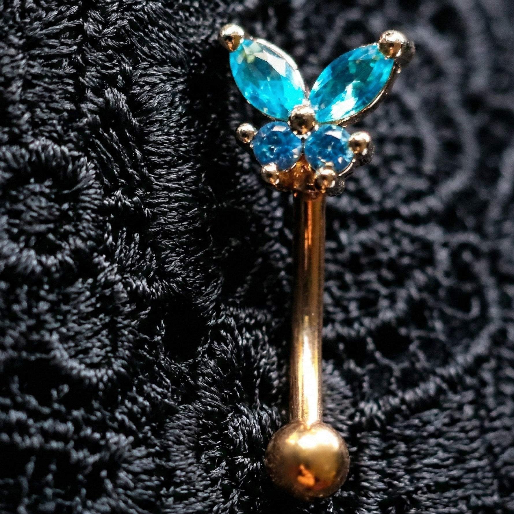Butterfly-shaped eyebrow piercing jewellery with blue gemstones on a textured black background