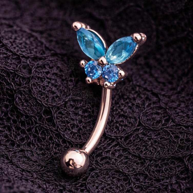 Butterfly-shaped eyebrow/rook bar with blue gemstones on a dark textured background