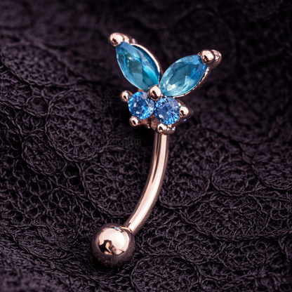 Butterfly-shaped eyebrow/rook bar with blue gemstones on a dark textured background