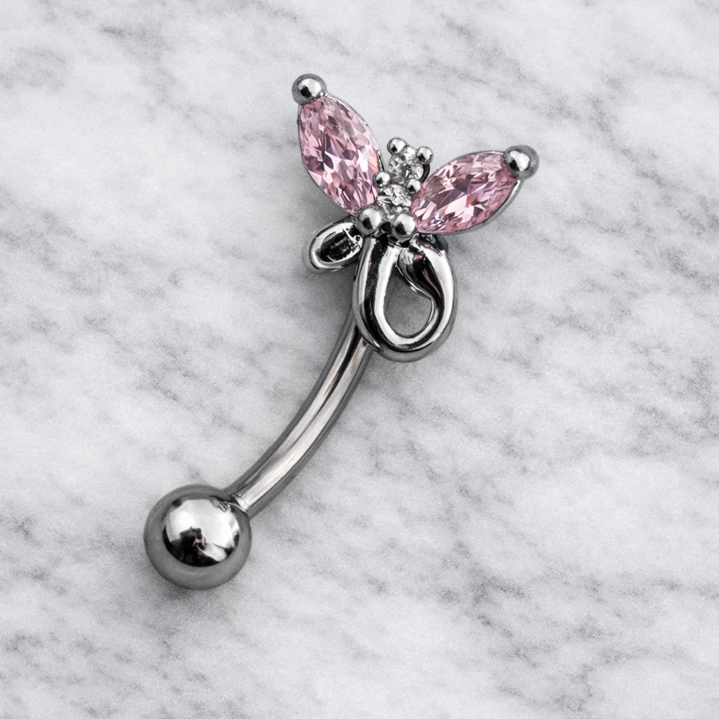 Butterfly-shaped eyebrow/rook bar with pink gemstones on a marble background