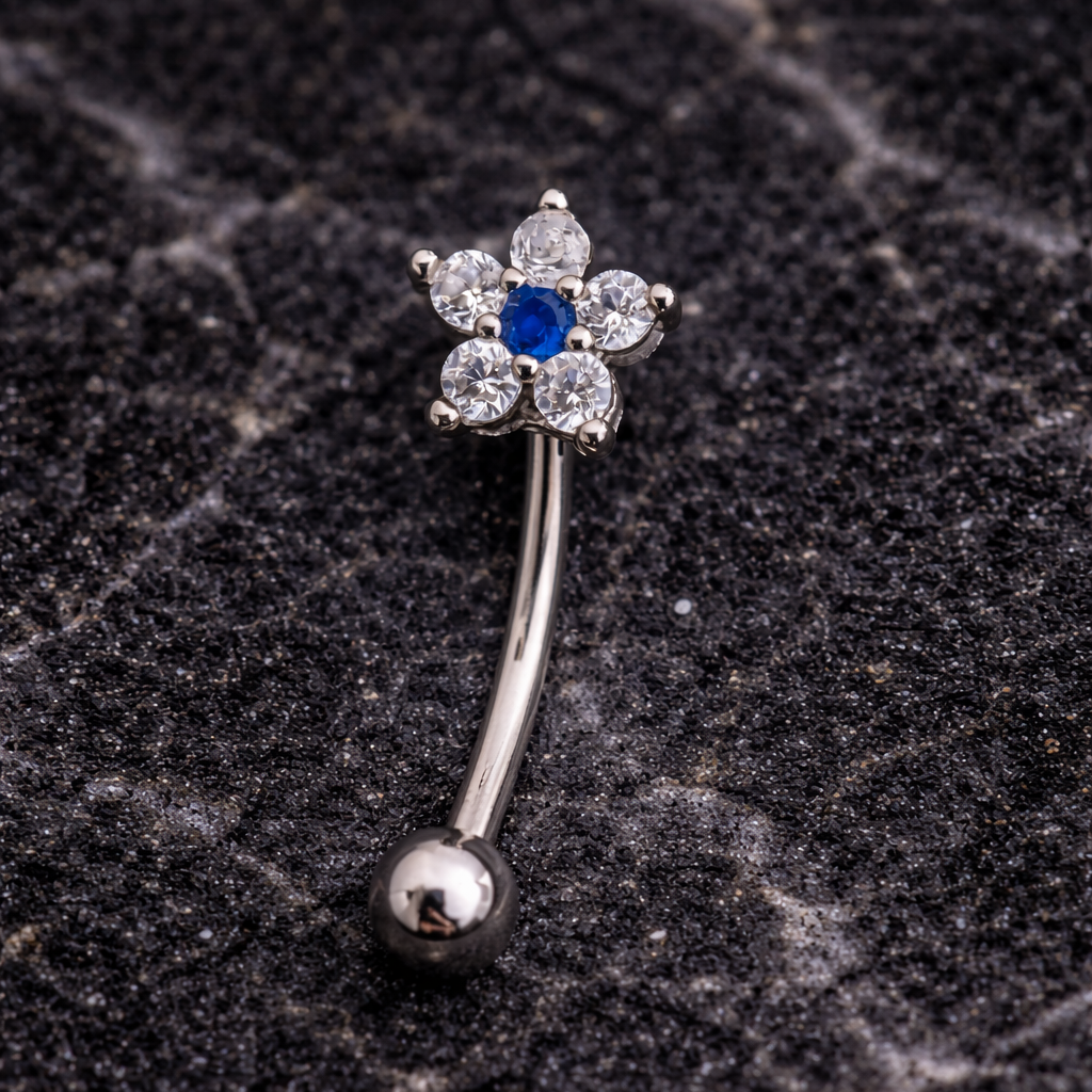 Silver eyebrow/rook bar with a blue gemstone on a dark textured surface