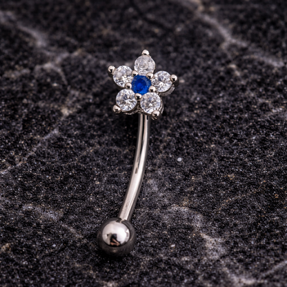 Silver eyebrow/rook bar with a blue gemstone on a dark textured surface
