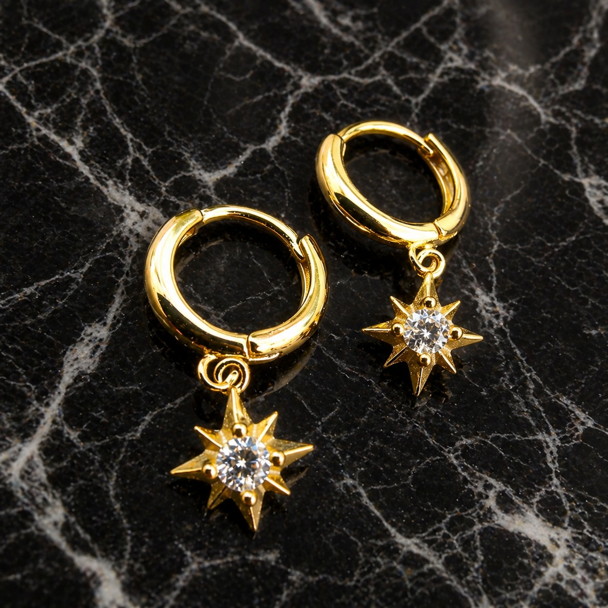 Gold hoop earrings with star-shaped charms on a black marble surface