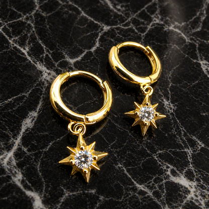 Gold hoop earrings with star-shaped charms on a black marble surface