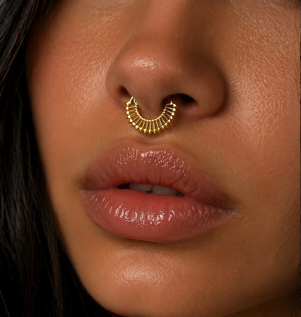 Close-up of a person wearing a gold nose ring with a dark background