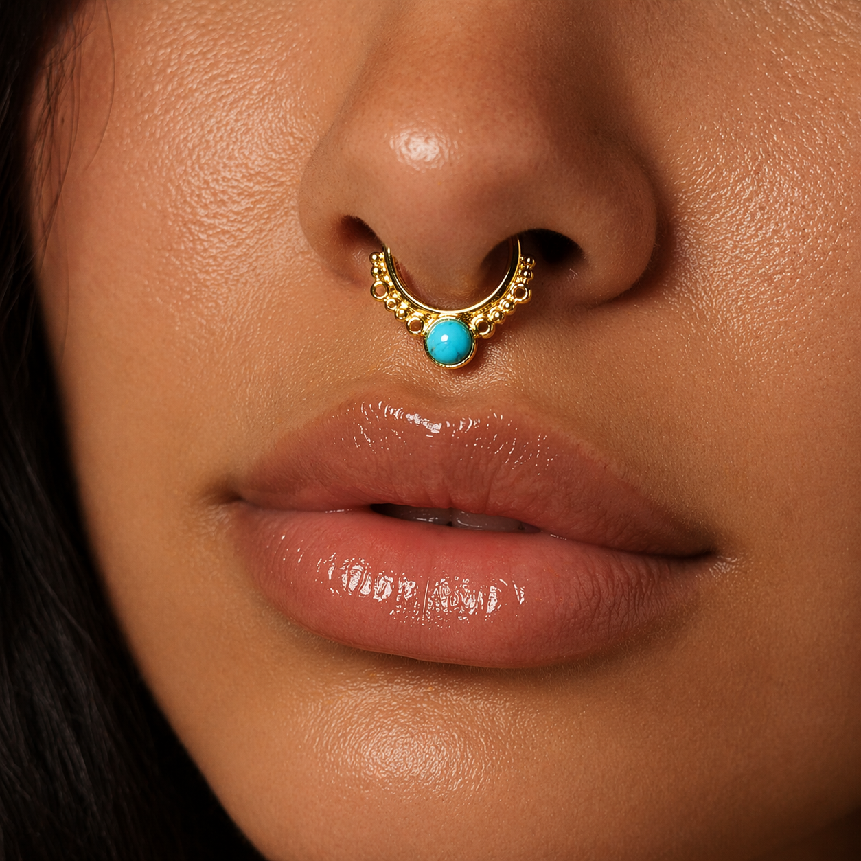 Close-up of a person wearing a gold nose ring with a turquoise stone.