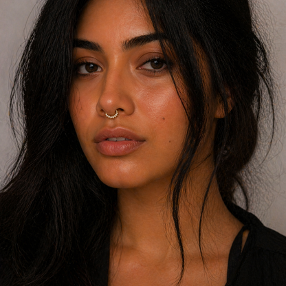 Close-up of a person with dark hair and a nose ring against a neutral background