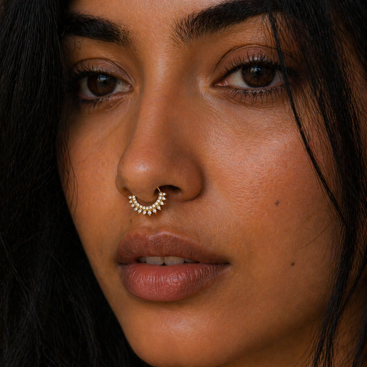 Close-up of a woman's face with a nose ring and dark hair.