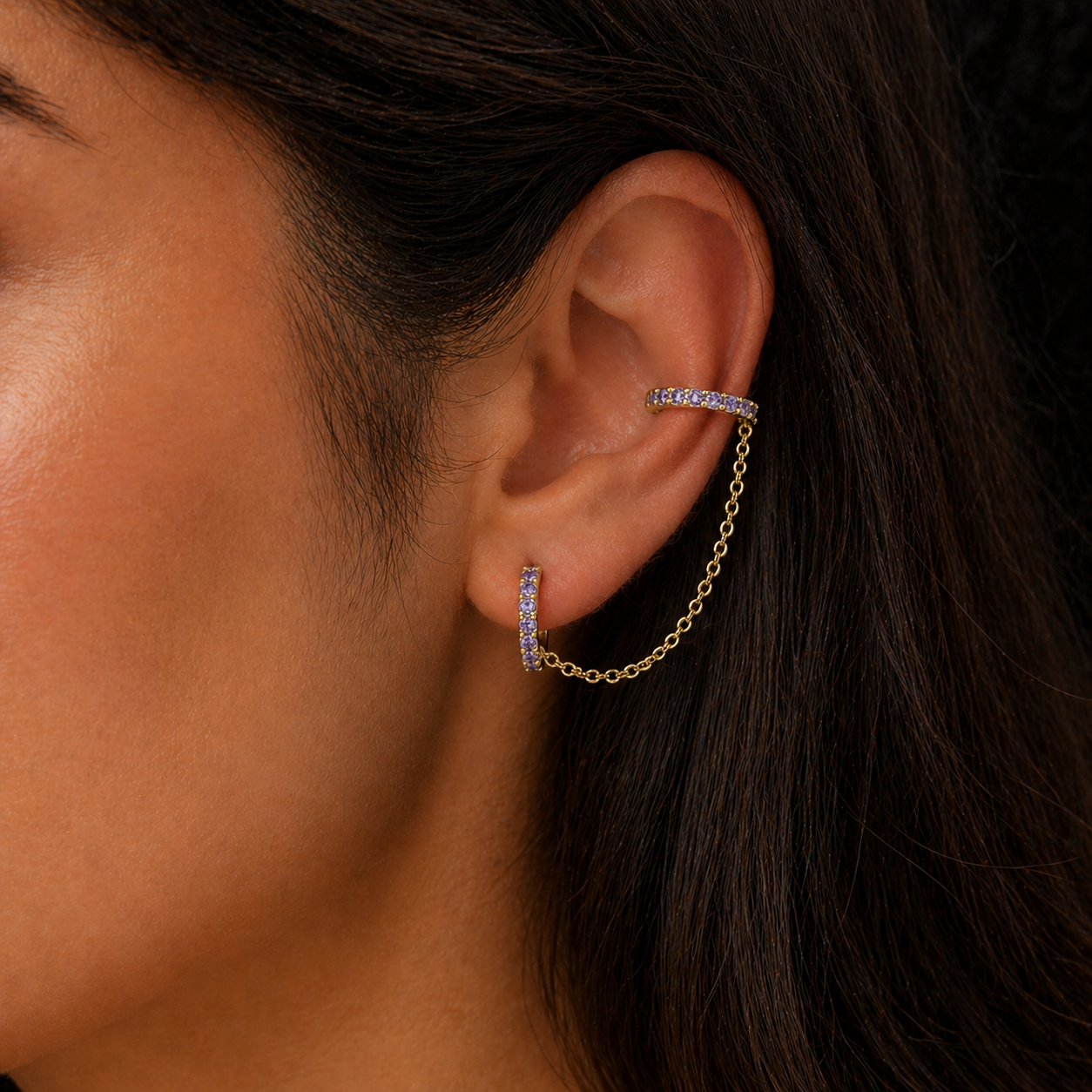 Close-up of an ear wearing a gold chain earring with purple gemstones.