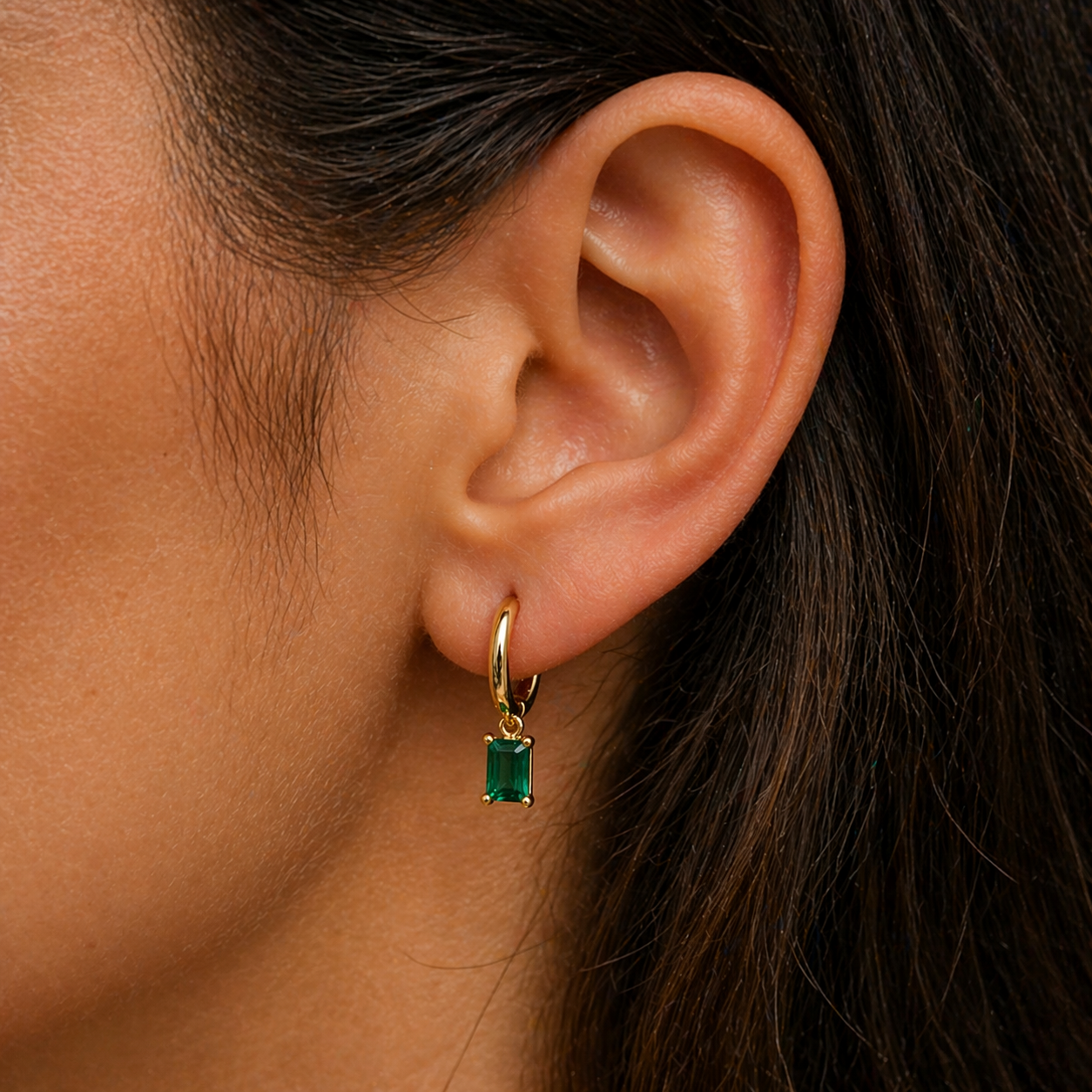 Close-up of an ear wearing a gold hoop earring with a green gemstone.