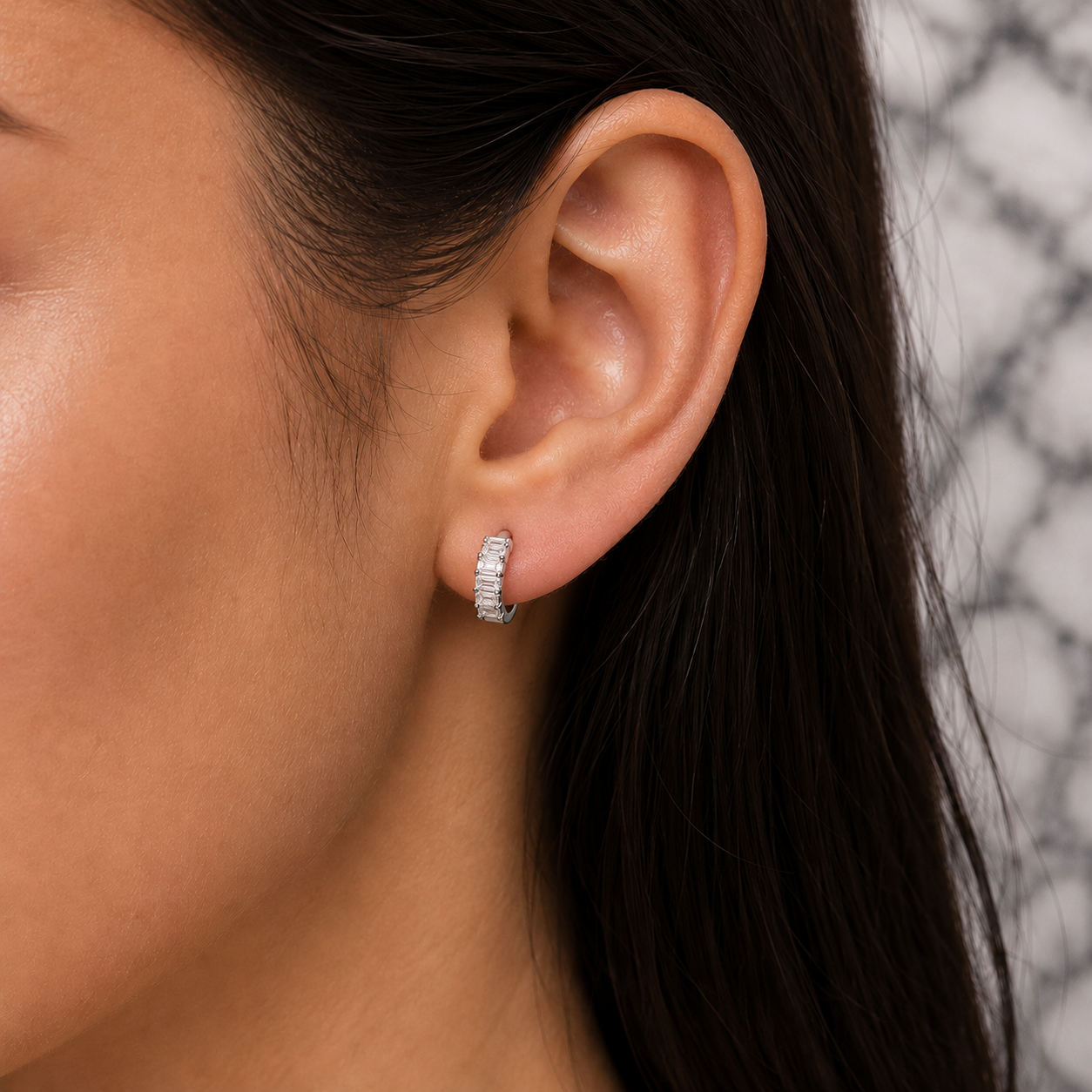 Close-up of an ear wearing a silver hoop earring with a blurred background
