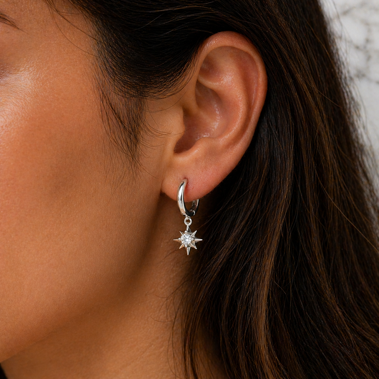 Close-up of an ear wearing a silver hoop earring with a star-shaped charm.