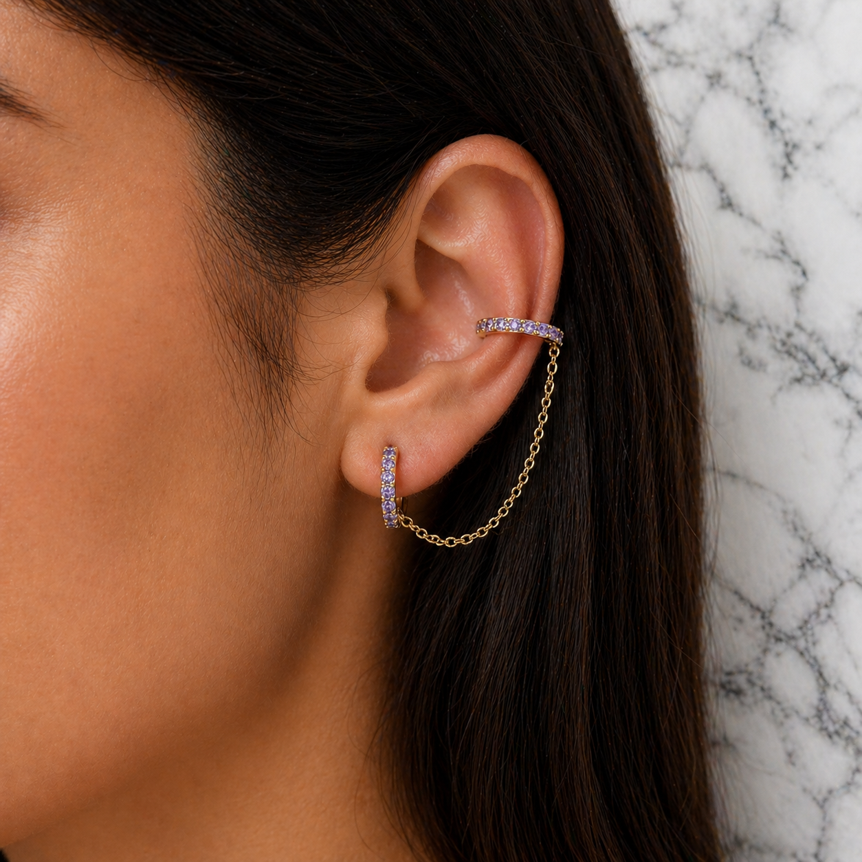 Close-up of an ear wearing gold and purple earrings against a marble background