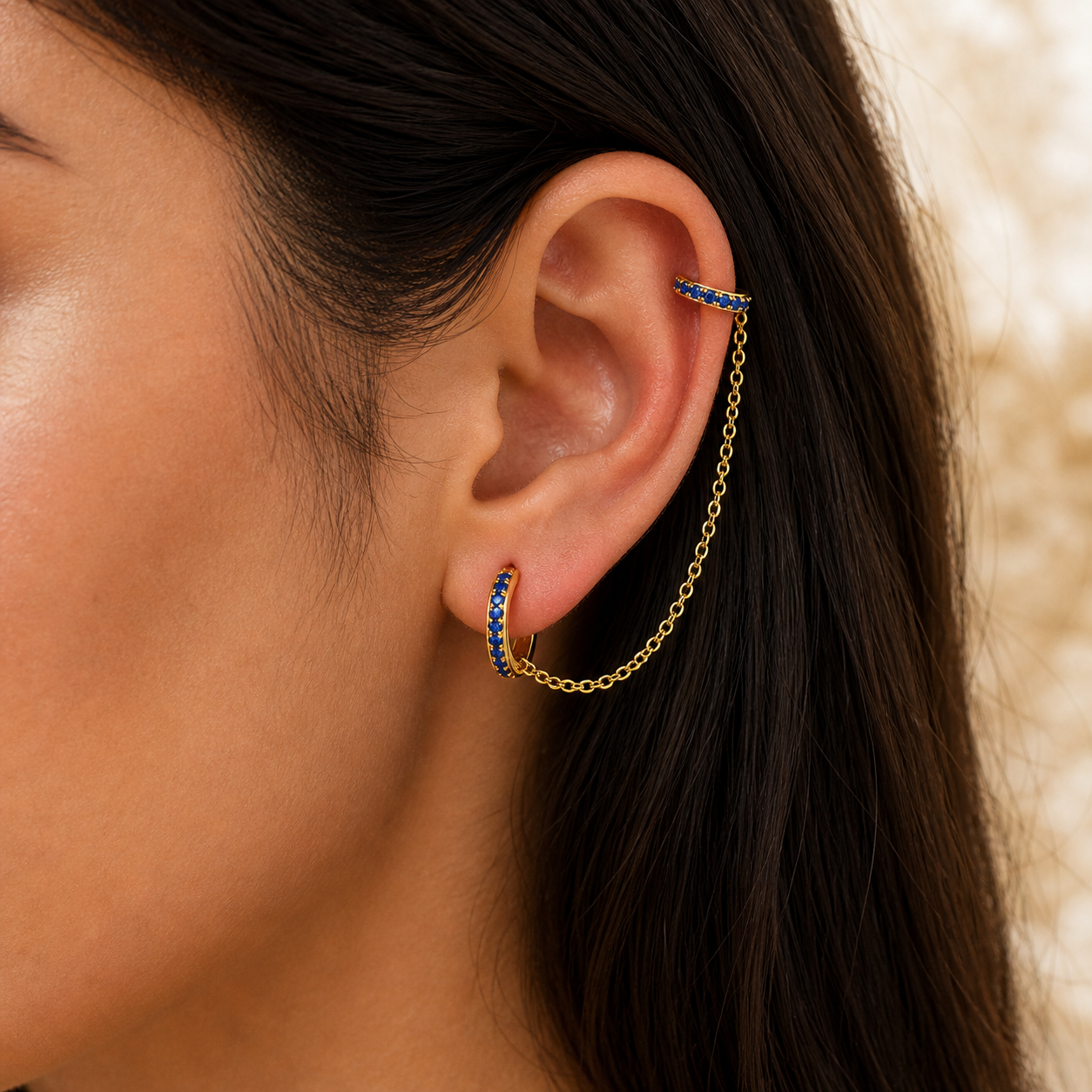 Close-up of an ear with gold chain earrings and blue gemstones.