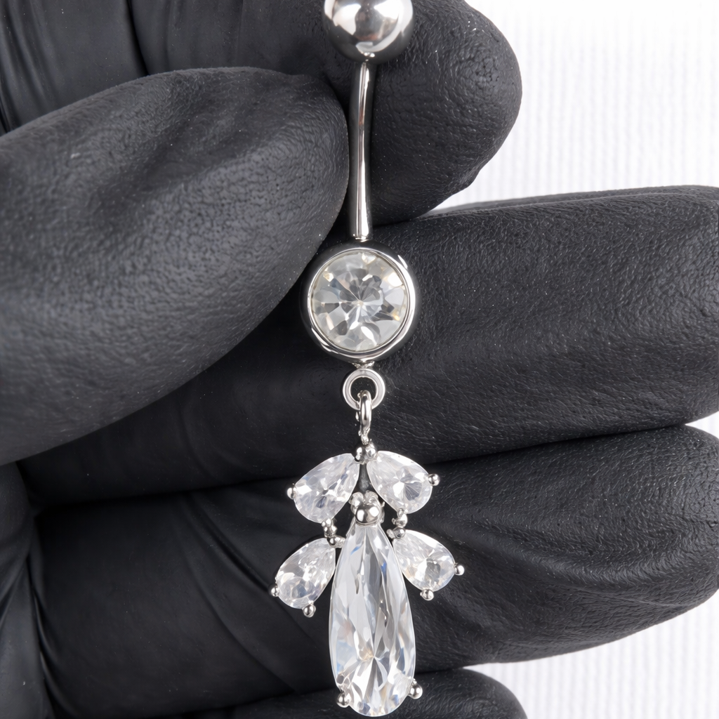 Belly button ring with clear gemstones held by a gloved hand on a white background