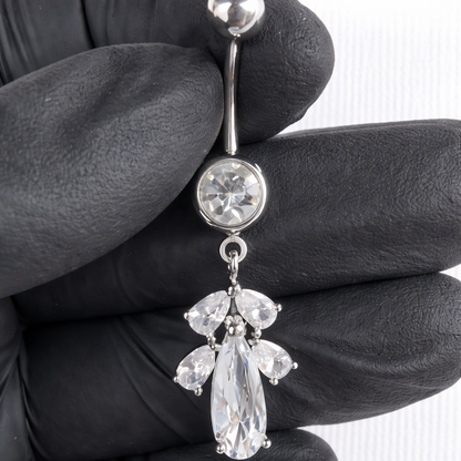 Belly button ring with clear gemstones held by a gloved hand on a white background