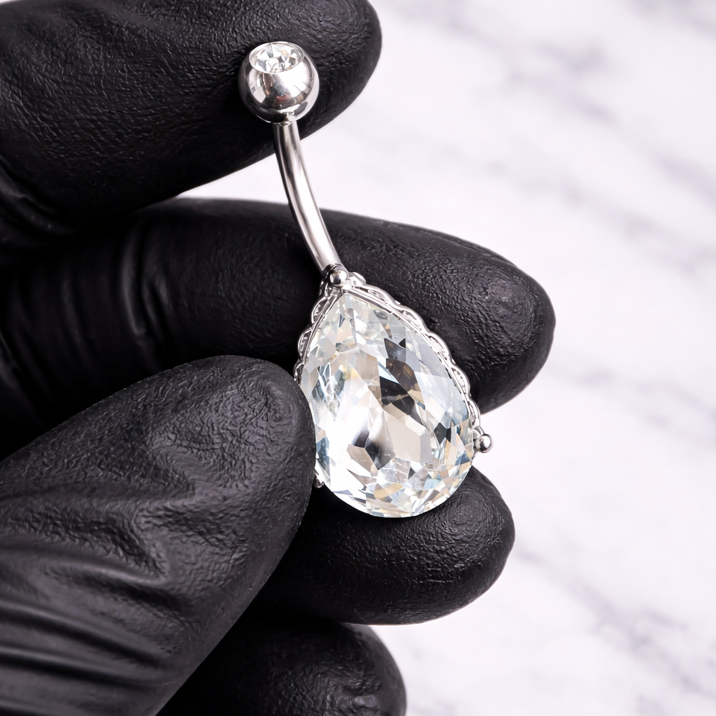 Pear-shaped diamond navel ring held by a gloved hand against a neutral background