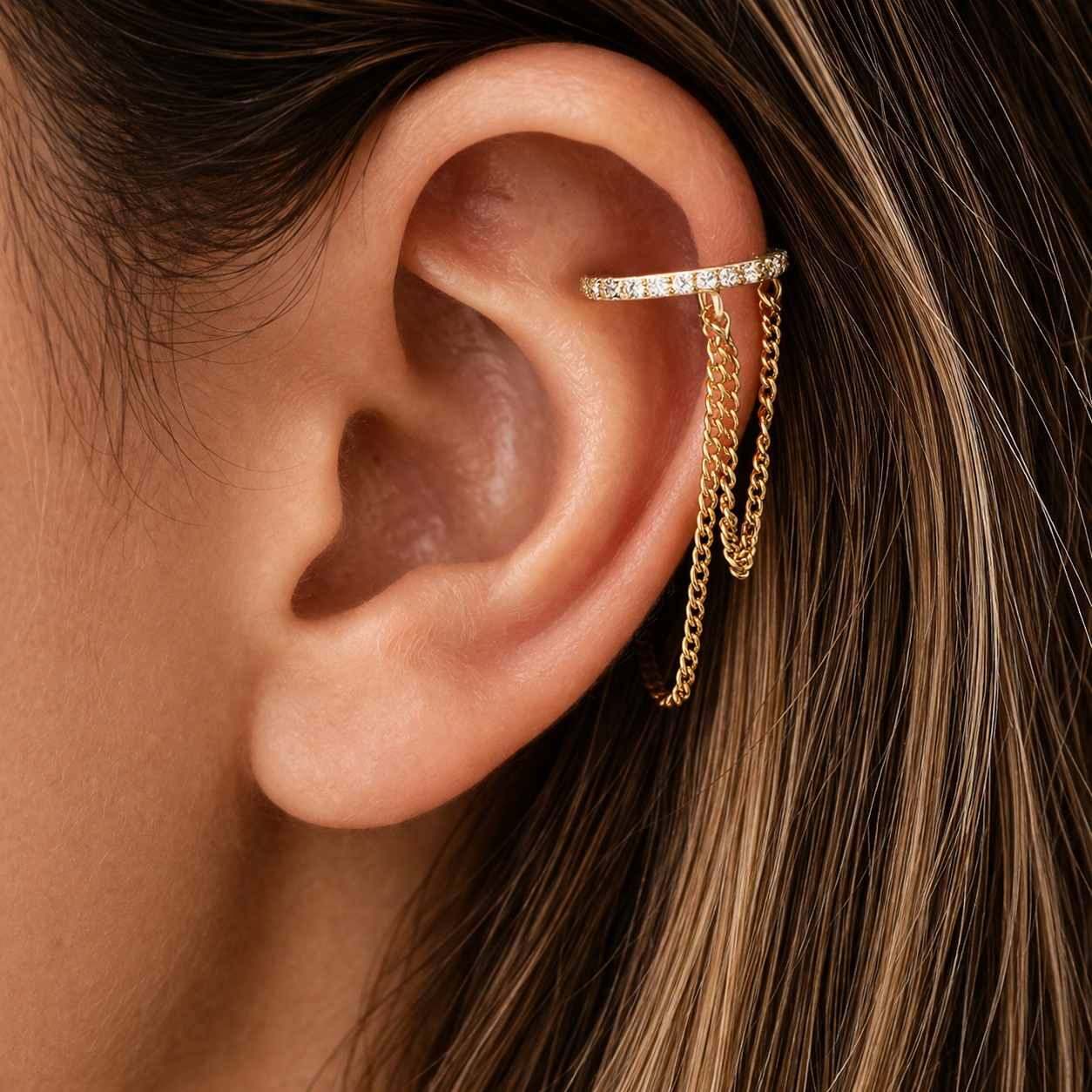 Close-up of an ear with gold chain earrings and a diamond ring on the earlobe.