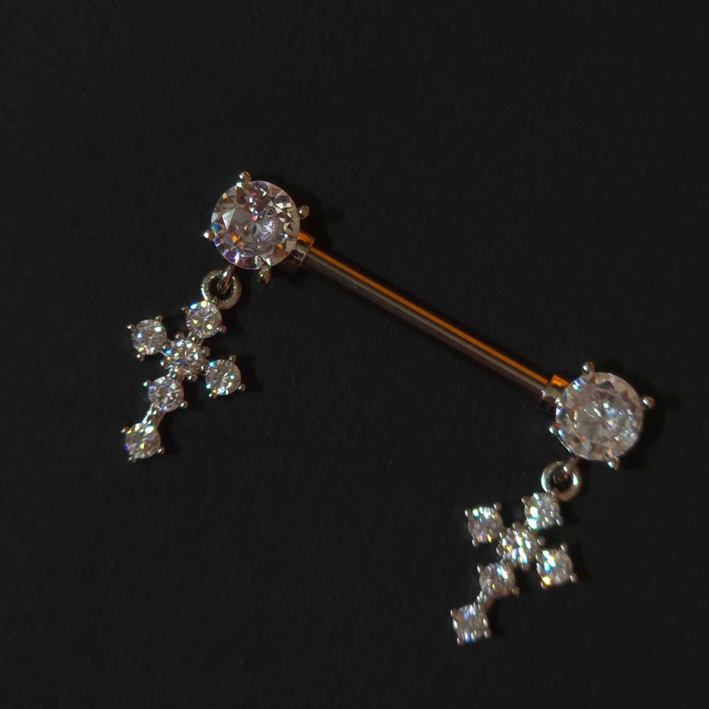 Diamond-studded cross nipple piercing barbells on a black background