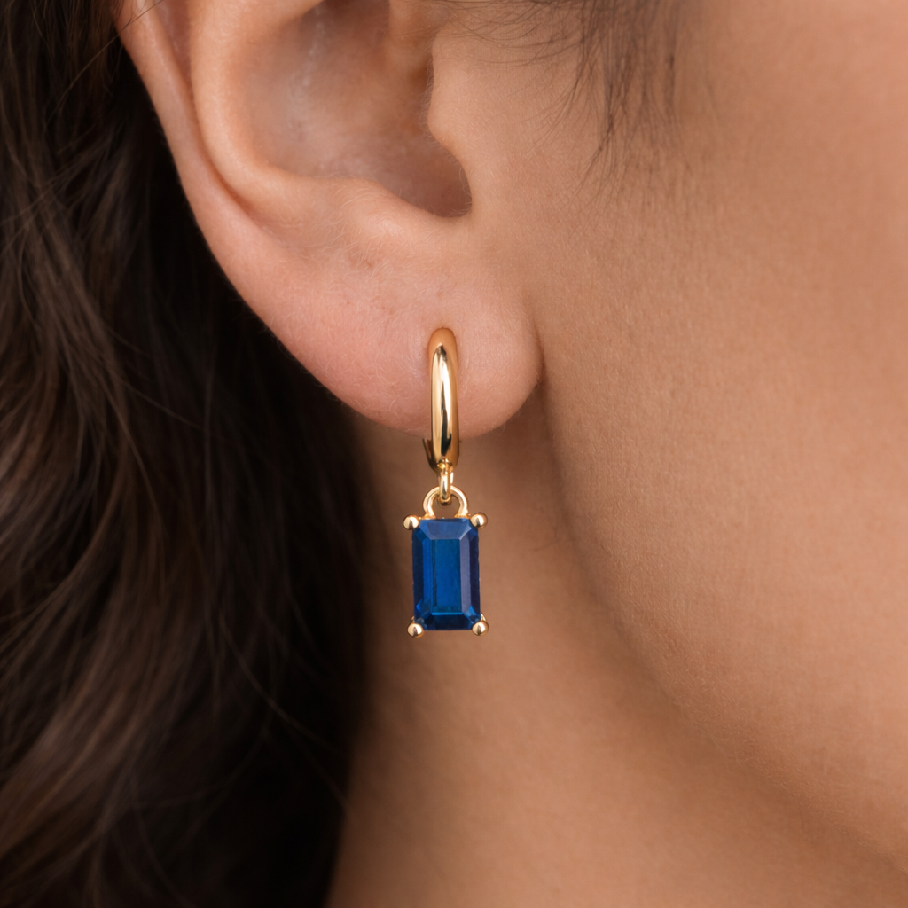 Gold earring with a blue gemstone worn by a person