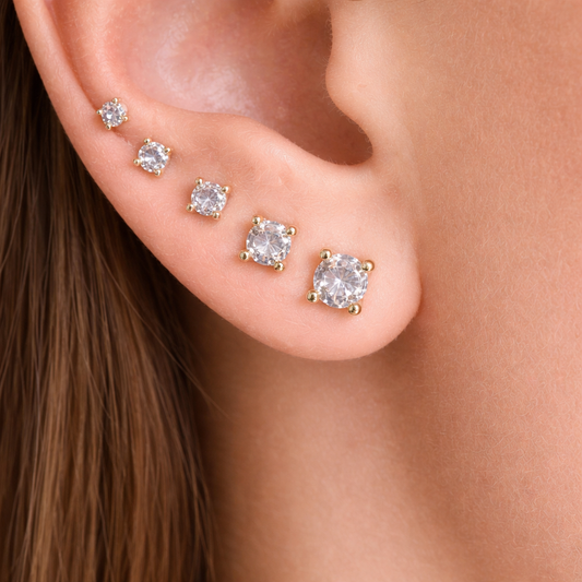 Close-up of an ear wearing gold earrings with clear gemstones.