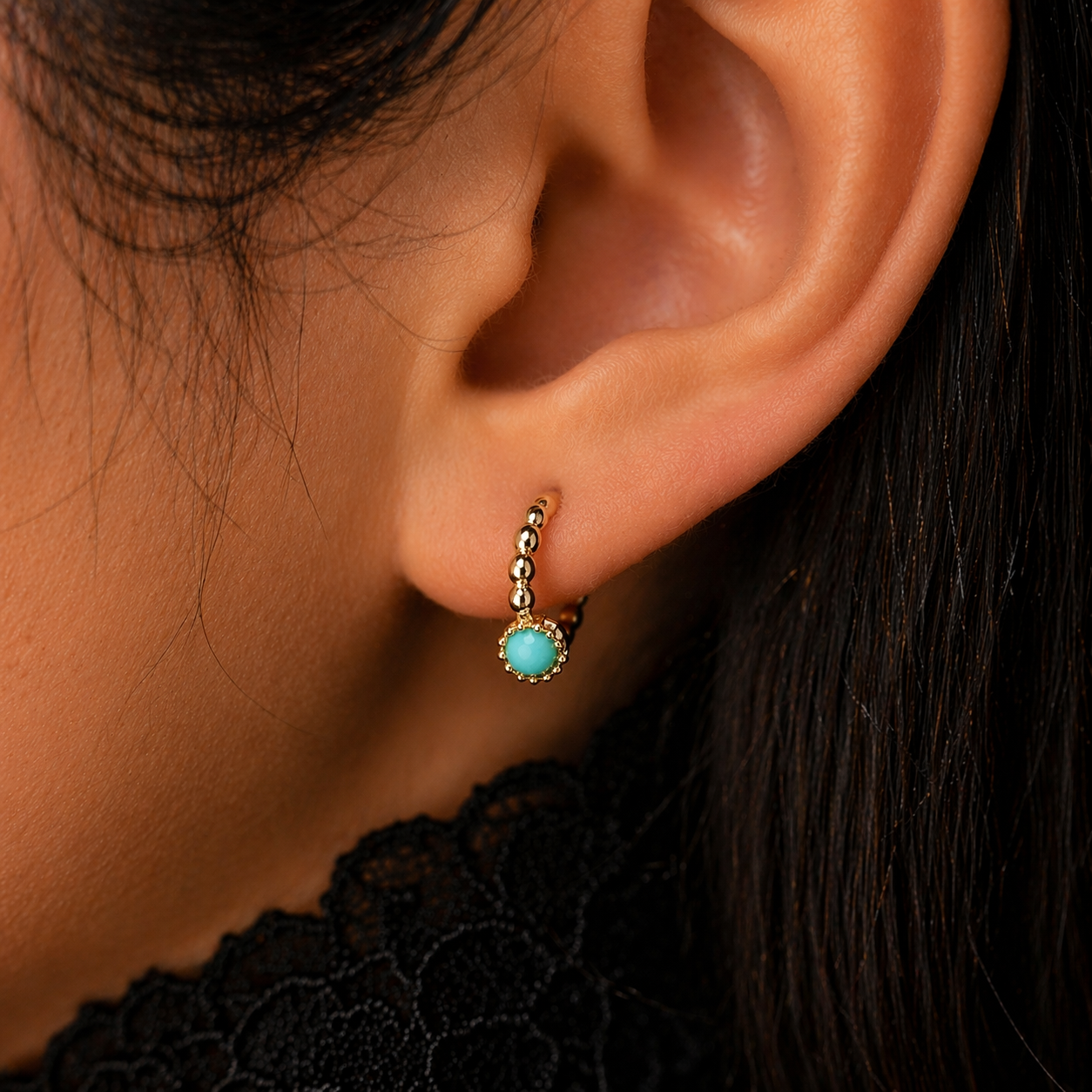 Close-up of an ear wearing a turquoise earring with gold accents.