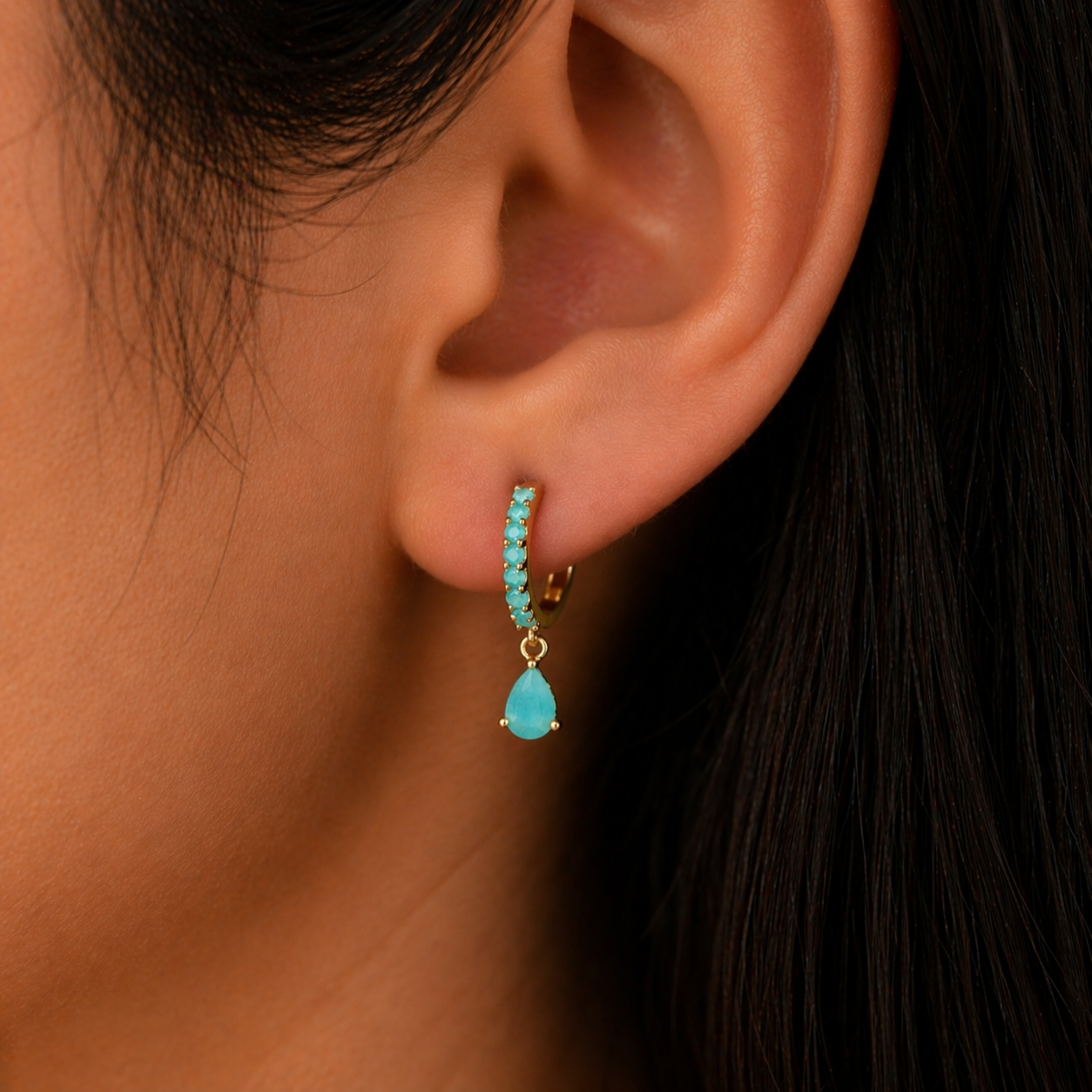 Close-up of an ear wearing turquoise earrings with dark hair in the background