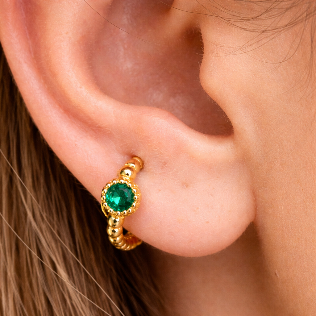 Gold earring with a green gemstone worn on an ear