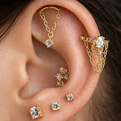Gold earrings with gemstones on an ear against a neutral background