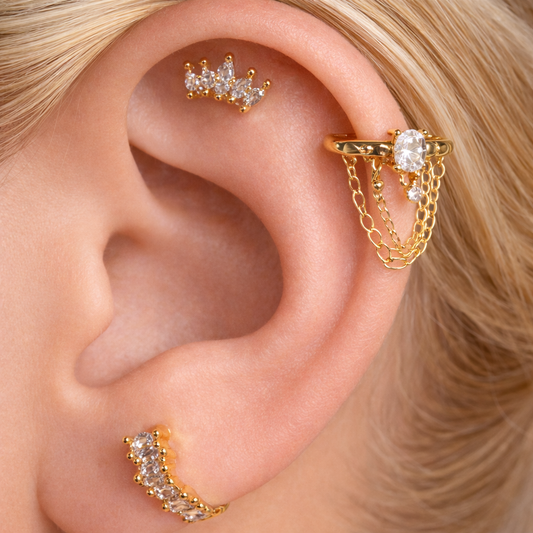 Gold earrings with clear gemstones worn on an ear