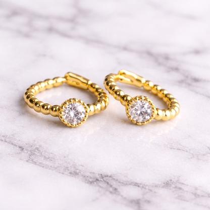 Gold hoop earrings with clear gemstones on a marble surface
