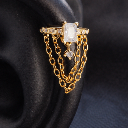 Gold ring with a large central gemstone and chain details on a dark background