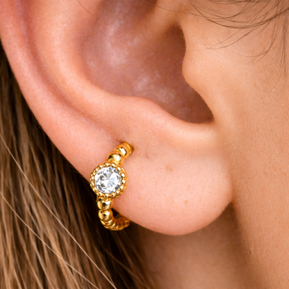 Gold earring with a clear gemstone worn by an ear