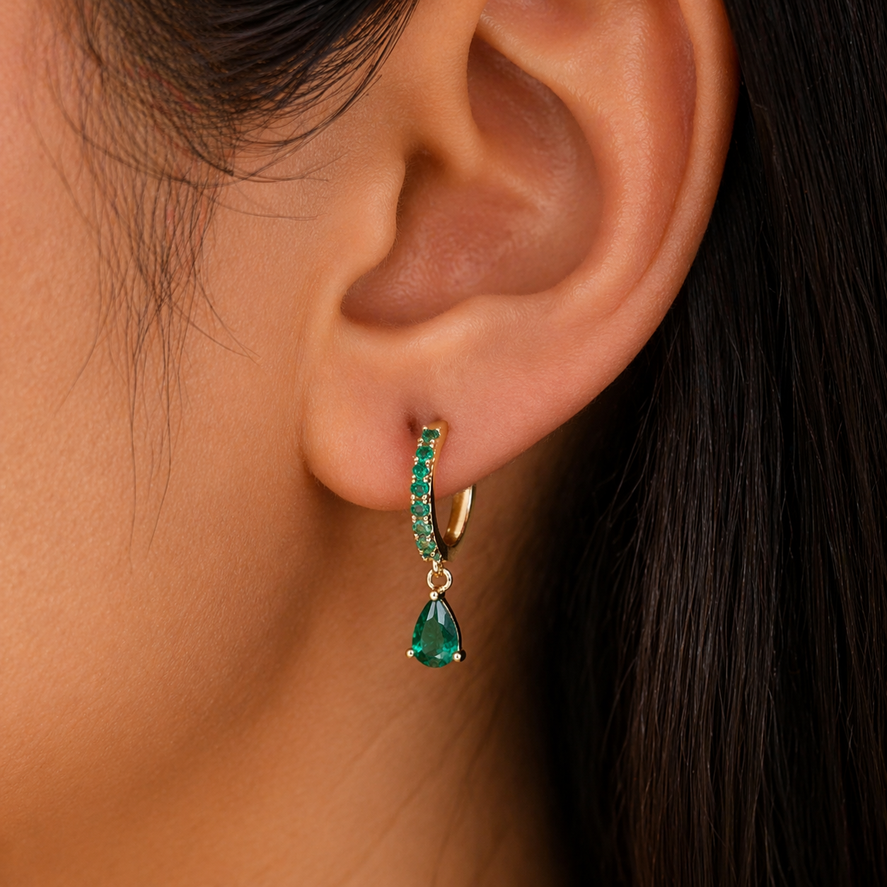 Close-up of an ear wearing a green teardrop earring with a blurred background