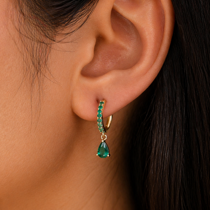 Close-up of an ear wearing a green teardrop earring with a blurred background