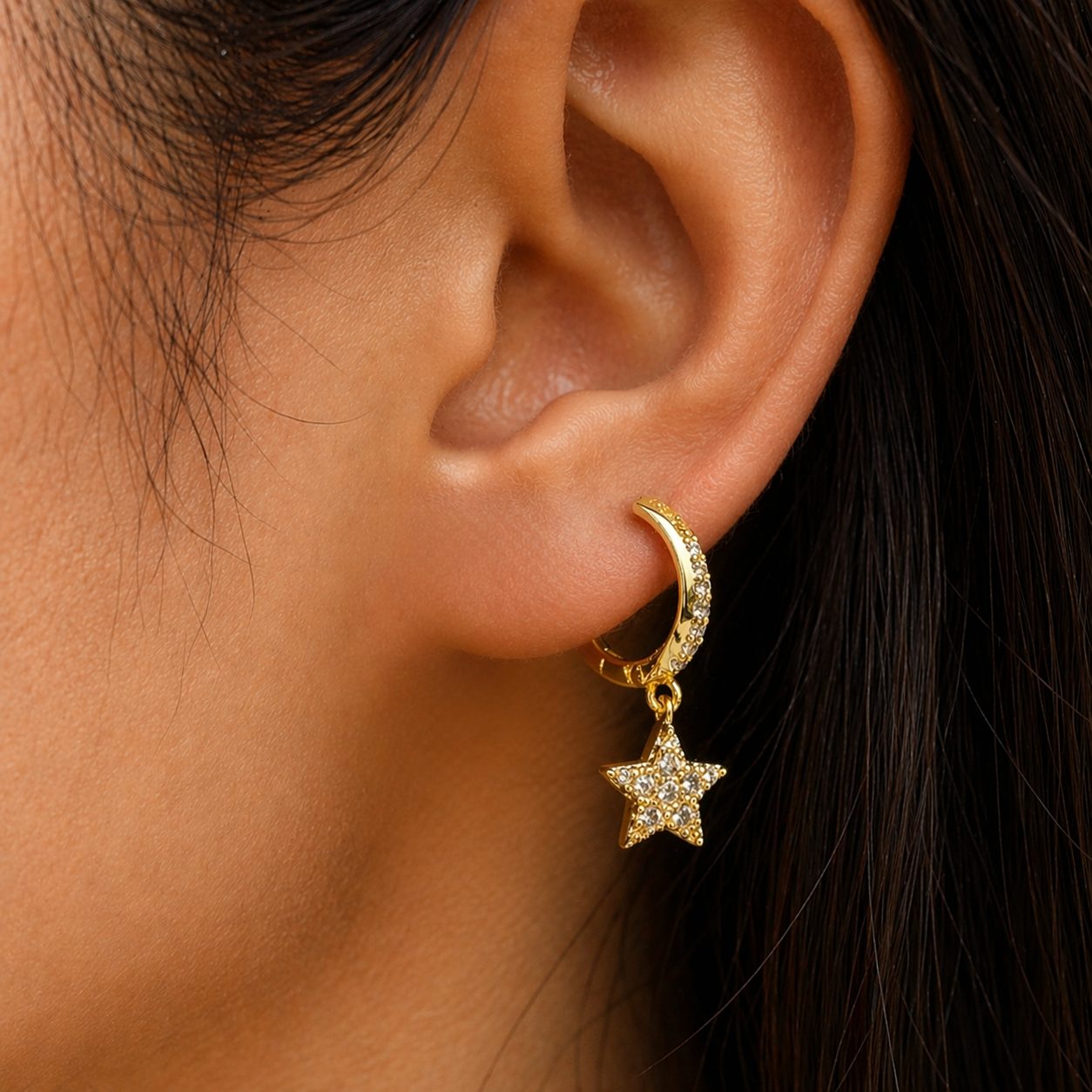 Close-up of an ear wearing a gold hoop earring with a star charm.