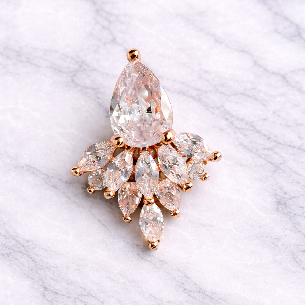 Rose gold belly ring with a central pear-shaped gemstone and smaller marquise-cut stones on a marble background