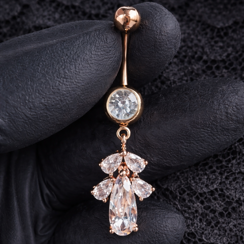 Diamante belly button ring held by a gloved hand against a dark background