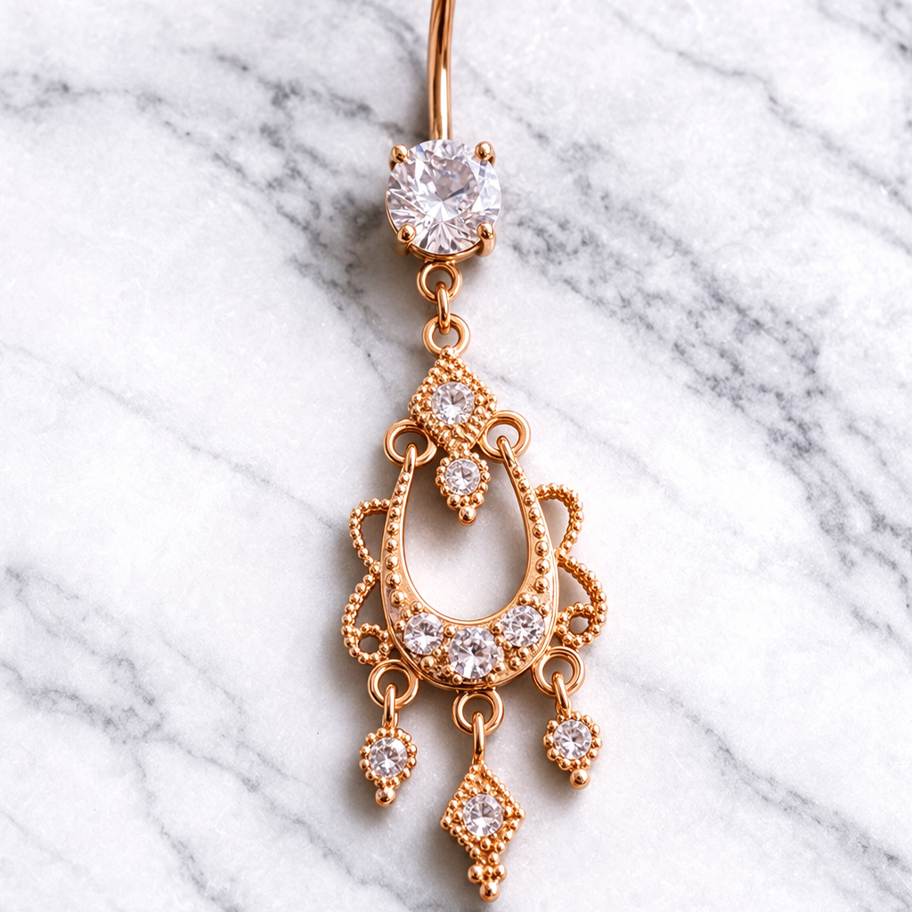 Rose gold belly button ring with decorative design on a marble background